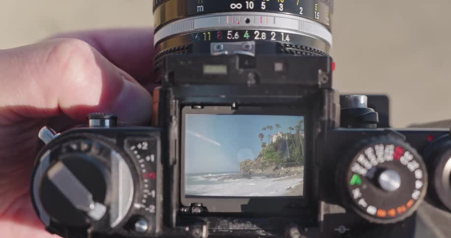 A photographer's point of view, looking through the waist-level viewfinder of a vintage film camera to frame a scenic coastal landscape