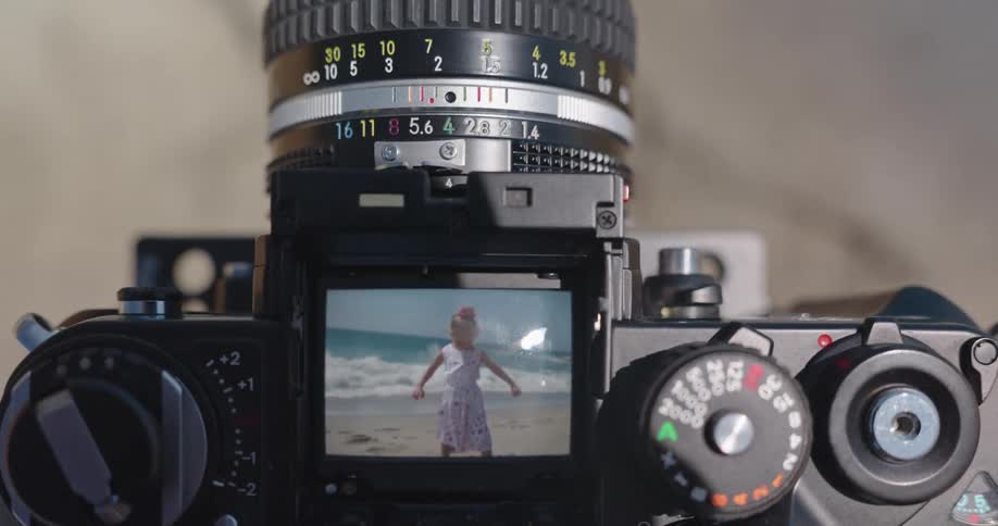 Looking through the viewfinder of a vintage film camera at a little girl posing by the ocean on a sunny beach