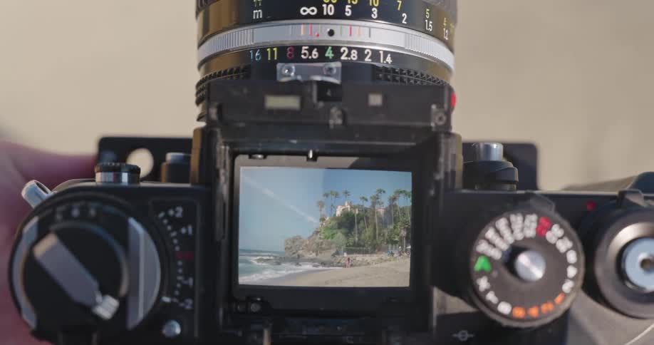 Looking through the top-down viewfinder of a vintage camera to frame a scenic shot of a sunny tropical beach with palm trees and ocean waves