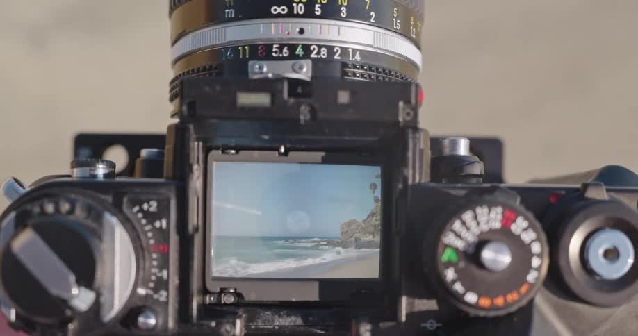 A close-up view through the viewfinder of a classic film camera captures a beautiful beach and ocean scene
