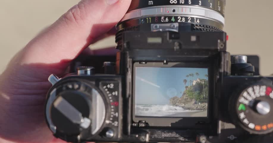 Looking through the viewfinder of a vintage film camera to frame a shot of a beautiful tropical beach with crashing waves