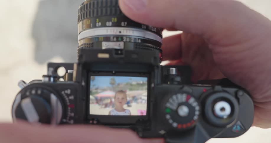 View through the viewfinder of a vintage SLR camera as a photographer focuses on a cute little girl on a sandy beach