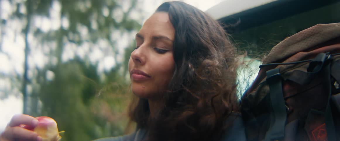 Close-up of a happy female traveler with wind in her hair eating a fresh apple