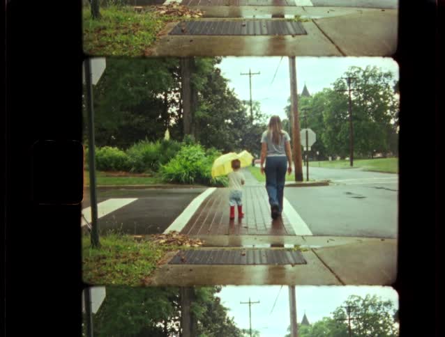 Archival footage shows a mother and child walking down a sidewalk on a rainy day, with the child holding a yellow umbrella