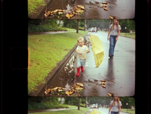 Vintage home movie footage shows a little boy in red rain boots splashing in puddles with a yellow umbrella after a storm