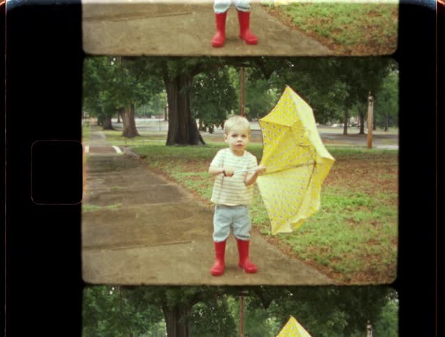Archival footage shows a cute little boy in red rain boots playing with a yellow umbrella in a park