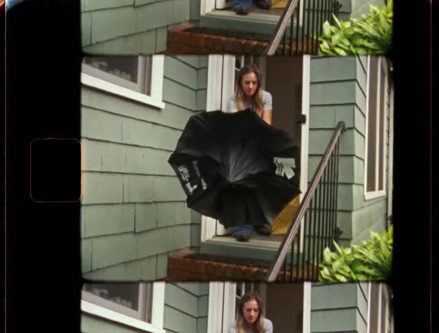 A young woman opens a black umbrella while standing in the doorway of a house in this vintage split-screen footage