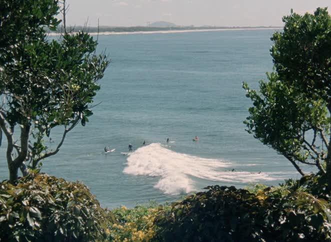 A vintage shot from a high vantage point shows surfers enjoying the waves in the vast blue ocean