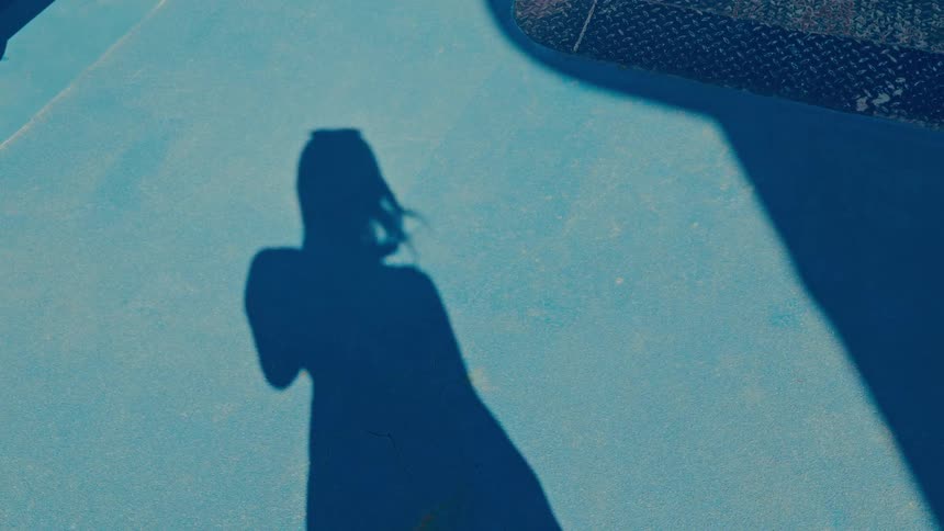 The shadow of a woman holding a phone is cast on a blue surface as her hair blows in the wind