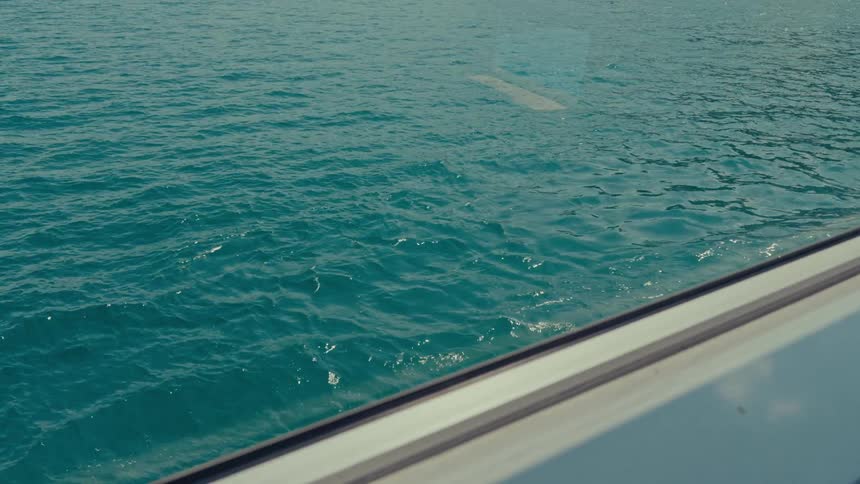 A calming slow-motion view of gentle turquoise sea waves rippling on a sunny day from inside a window