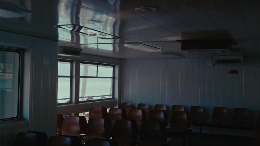 The dimly lit and deserted passenger lounge of a ferry boat as it travels across the sea