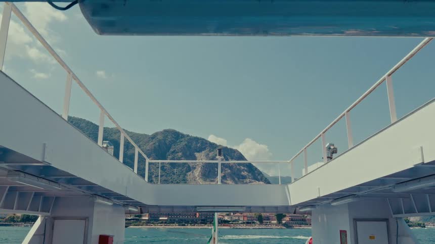 A scenic point-of-view from a ferry sailing towards a mountainous coastline on a beautiful sunny day