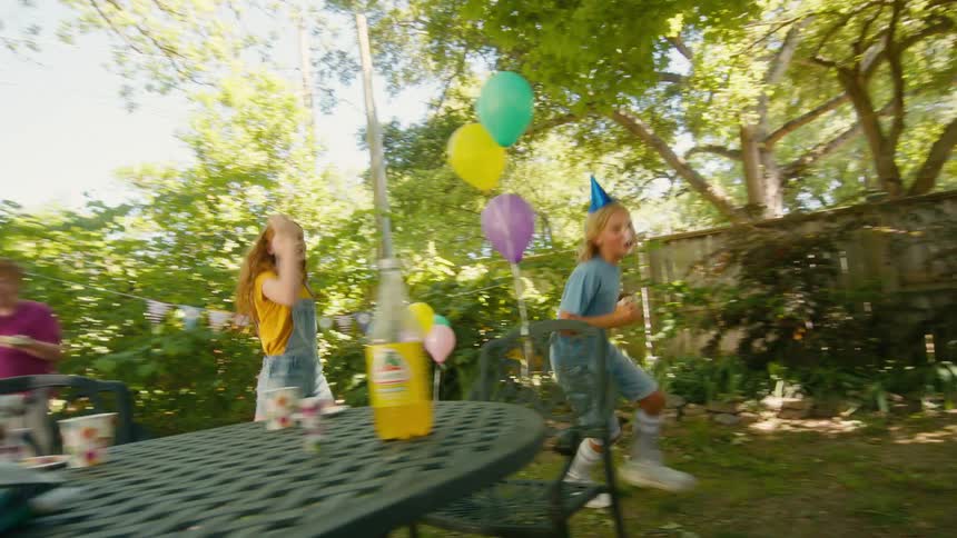 A boy with cake on his face joyfully runs around a backyard birthday party