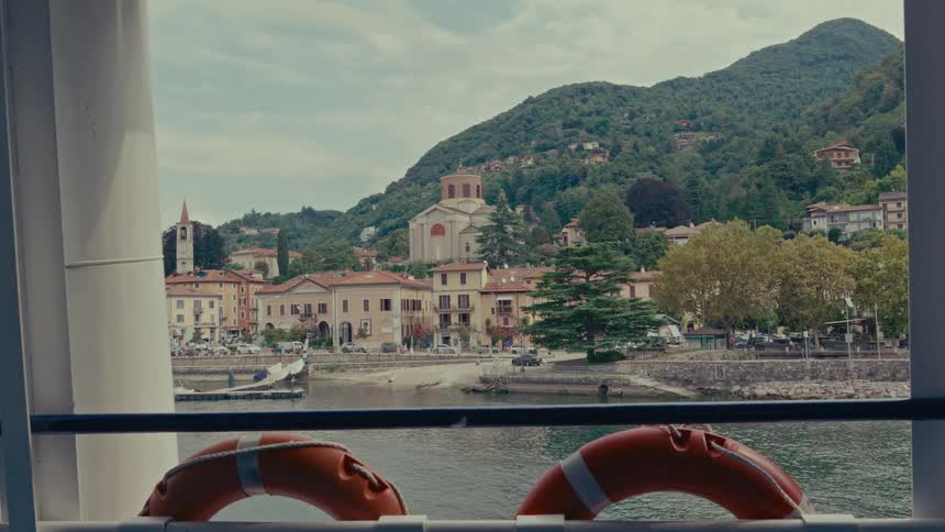 A picturesque view of a charming Italian lakeside town nestled at the foot of green mountains, seen from a boat on the water