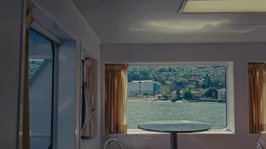 A picturesque view of a sunny European lakeside town from the calm interior of a moving ferry