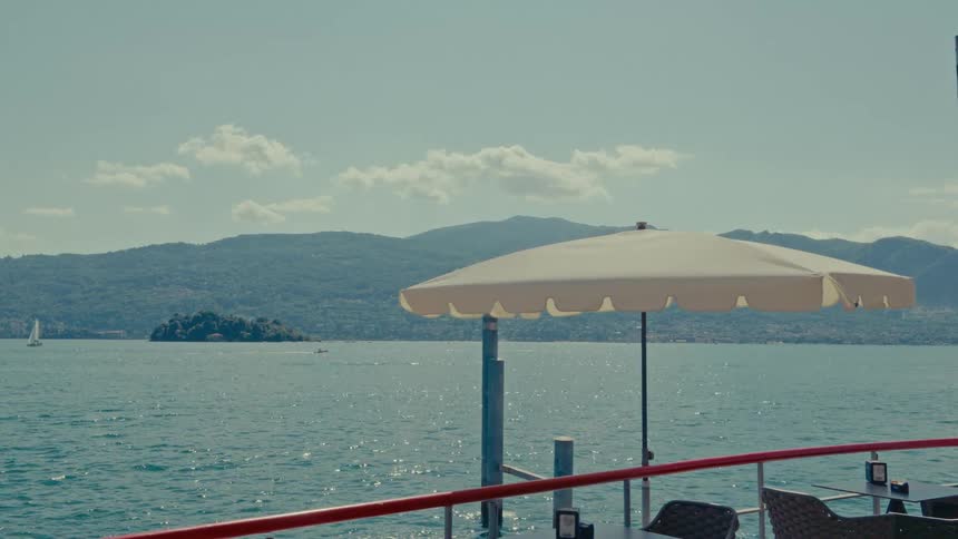 A relaxing view from a lakeside cafe patio with an umbrella overlooking a sparkling lake and distant mountains on a sunny day