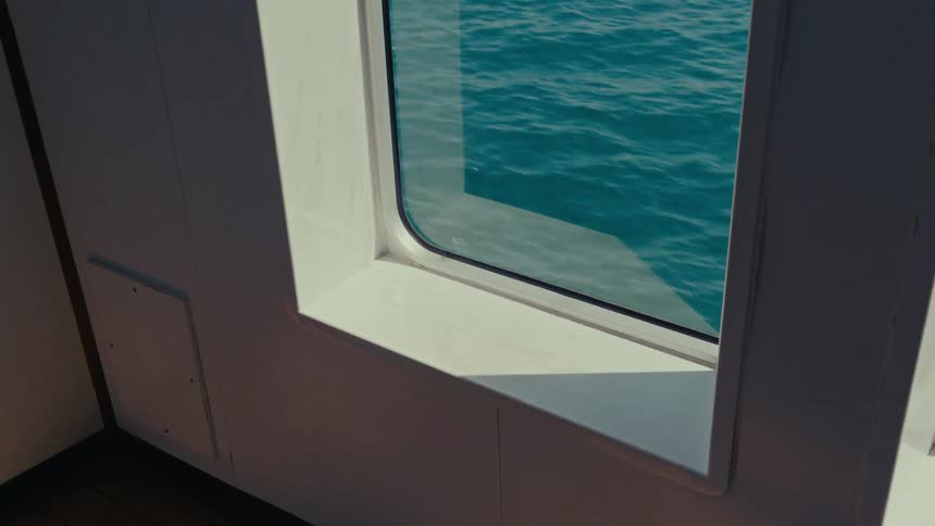 The calm, turquoise ocean passes by a boat's window on a tranquil, sunny day