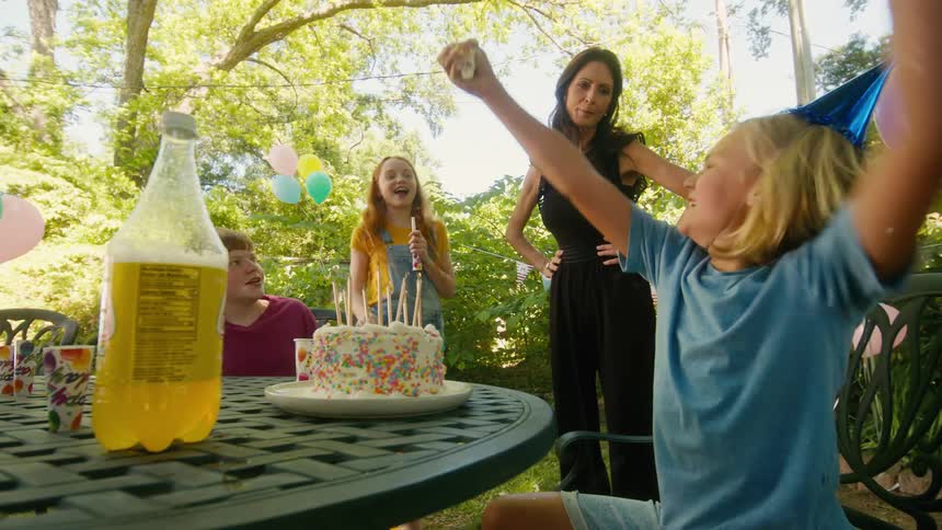 An excited birthday boy celebrates with friends and family in the backyard, eagerly grabbing a handful of his cake