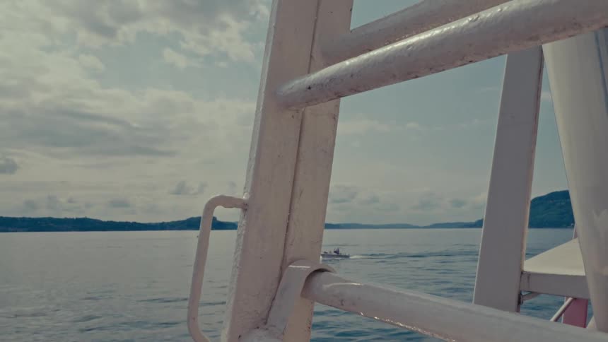 A view from the side of a boat reveals a small motorboat cruising across the calm water on a partly cloudy day