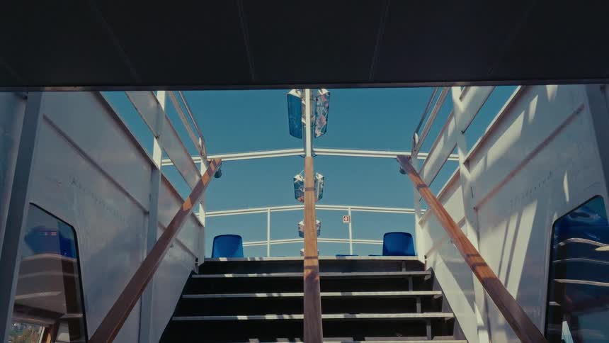 A slow pull-out shot from inside a ferry, looking up the stairs to the sunny, empty upper deck