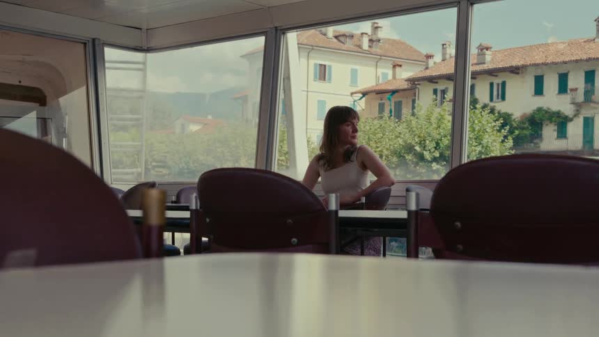 A thoughtful woman sitting alone on a ferry looks out the window at a picturesque European town