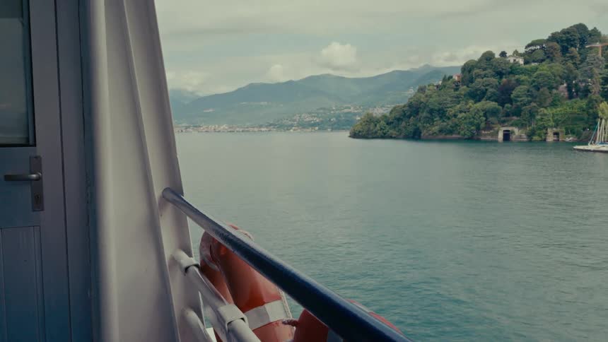 A tranquil boat ride on a lake, passing by lush green hillsides and a marina under a cloudy sky