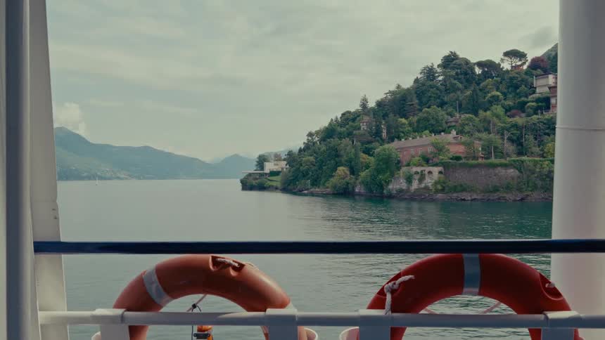 Scenic view of a lush green shoreline on a vast lake, as seen from the deck of a ferry with lifebuoys in the foreground