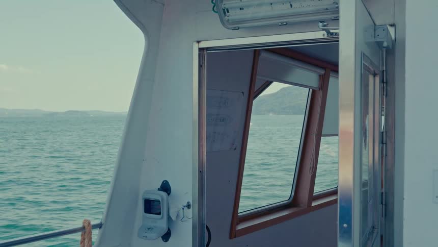 A serene view of the open sea and distant land from the side of a boat looking into the cabin