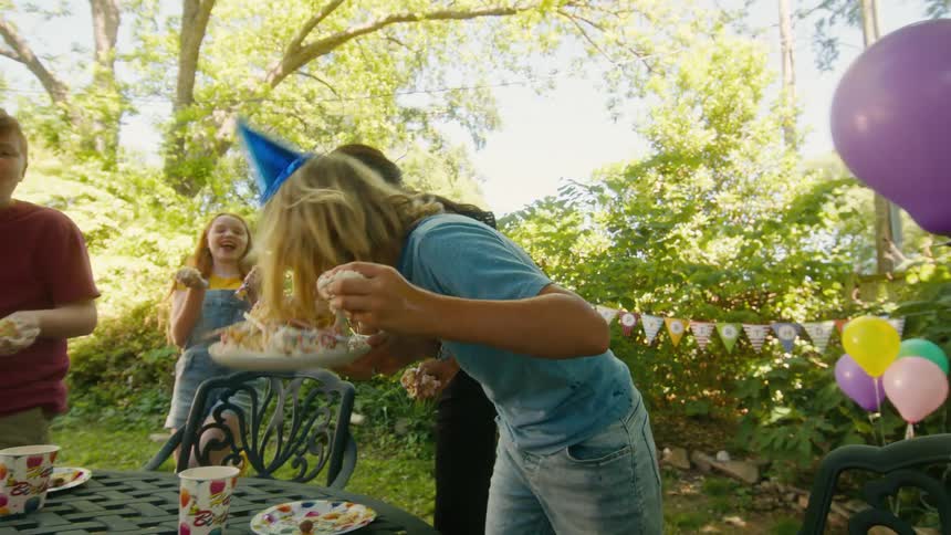 Kids having a wild and messy time eating birthday cake with their hands at an outdoor party