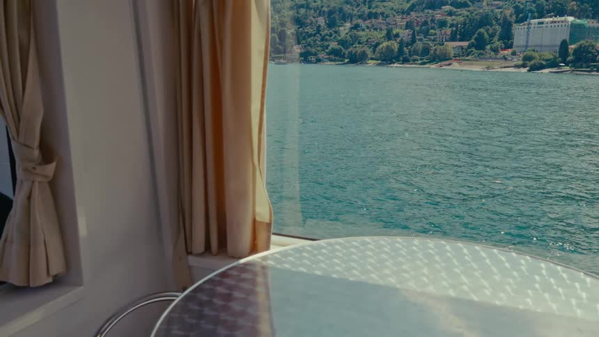 A serene view from a boat window overlooks the glistening water as the scenic shoreline passes by on a sunny day