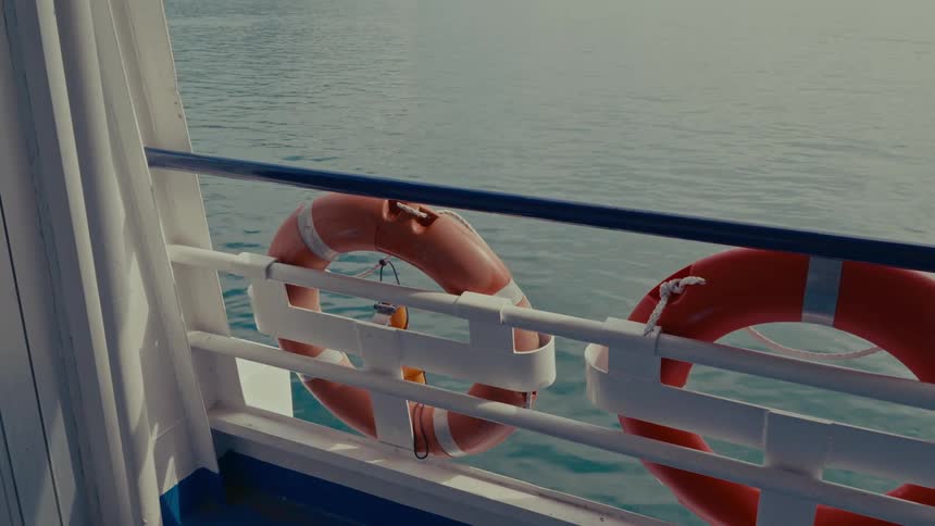 Lifebuoys attached to the railing of a ferry sailing across the calm sea on a sunny day