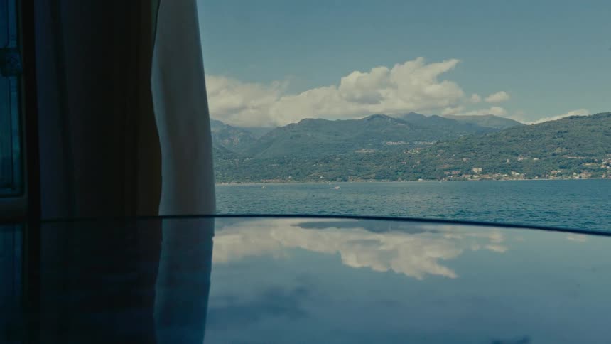 A scenic view from a boat shows the reflection of the sky on its glossy roof, with a beautiful mountainous coastline in the distance
