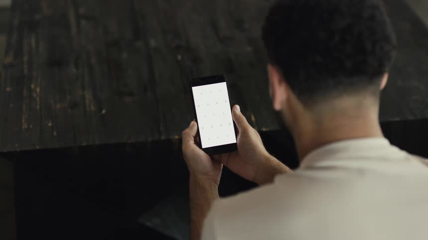 Over the shoulder view of a man holding a smartphone with a white screen and tracking markers, perfect for compositing