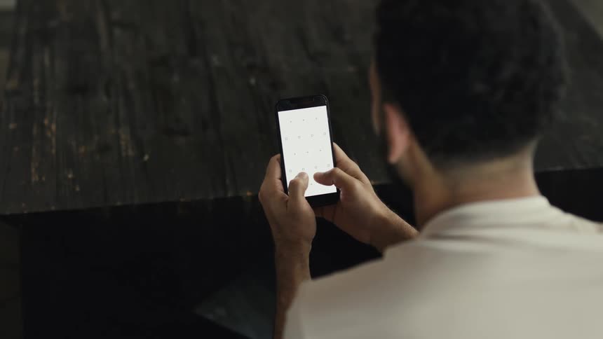 Over-the-shoulder view of a man using a smartphone with a blank white screen with tracking markers, ideal for content insertion