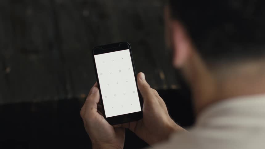 Over the shoulder view of a man holding a smartphone with a blank white screen and tracking markers