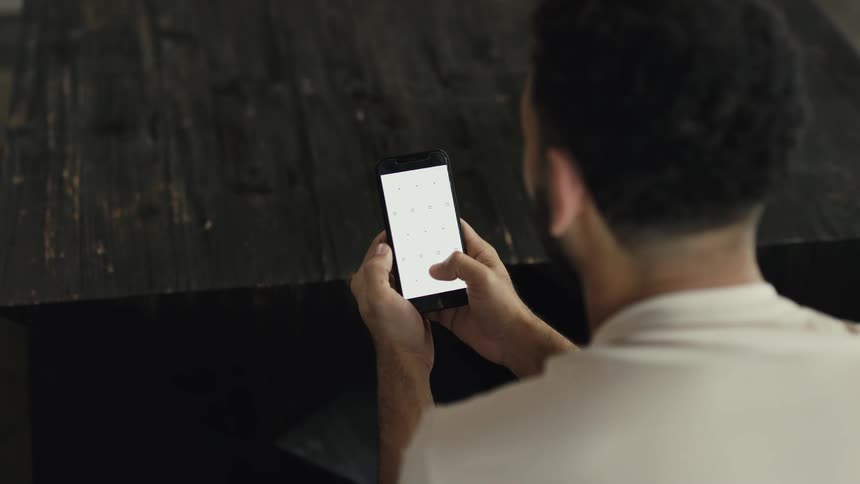 Over the shoulder shot of a man holding and using a smartphone with a blank screen featuring tracking markers