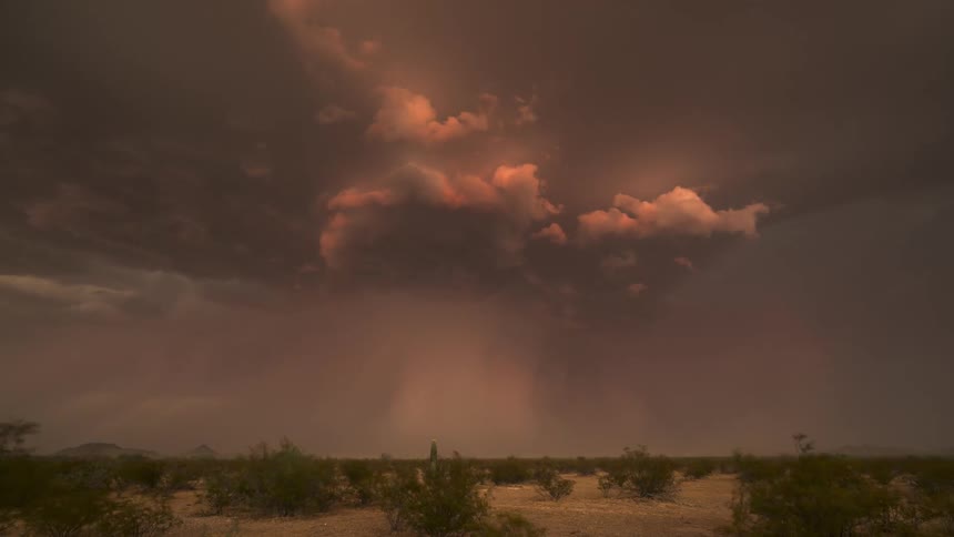 A dramatic timelapse captures an ominous desert thunderstorm with a powerful microburst and flashes of lightning under an apocalyptic, orange-hued sky