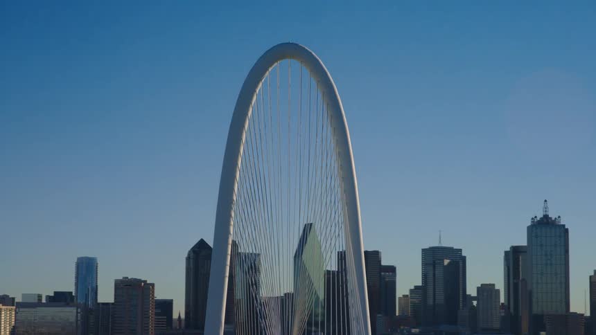 An aerial view pulls back from the iconic Margaret Hunt Hill Bridge to reveal the downtown Dallas, Texas skyline on a clear day