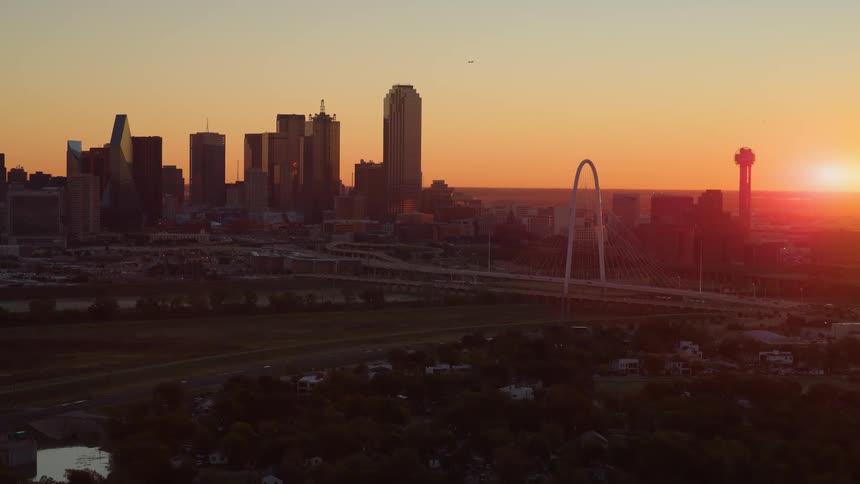 Aerial view of the Dallas, Texas skyline as the sun rises, casting a beautiful orange glow over the city
