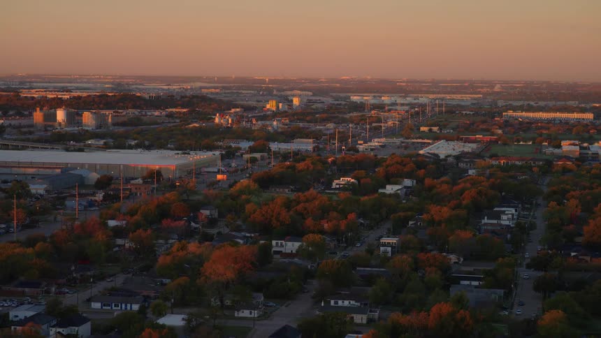 An expansive aerial view captures a blend of residential neighborhoods and industrial complexes under the warm, golden light of sunset