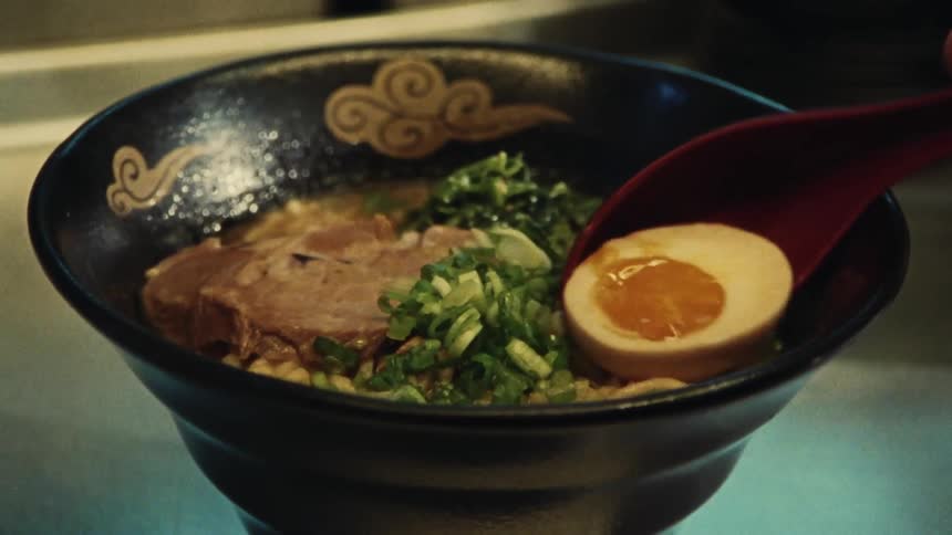 A soft-boiled egg is placed into a bowl of traditional Japanese ramen in slow motion