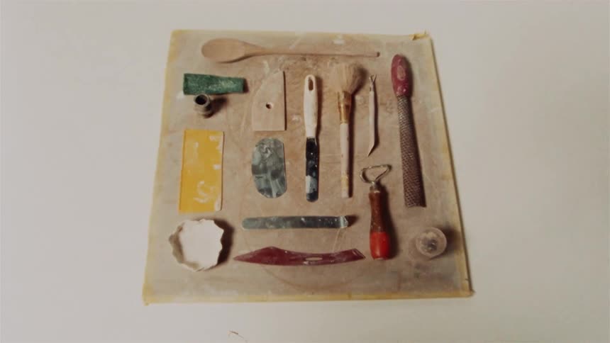 An overhead view slowly zooms out from a flat lay of various well-used pottery and sculpting tools