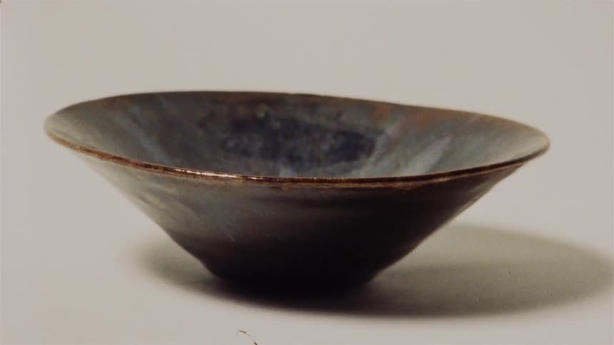 A stop-motion collection of various handmade ceramic bowls displayed on a white background before a hand gently wipes one clean