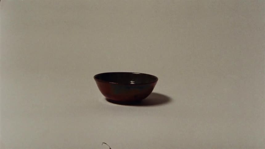 A minimalist still life of a handcrafted ceramic bowl slowly being illuminated against a plain background