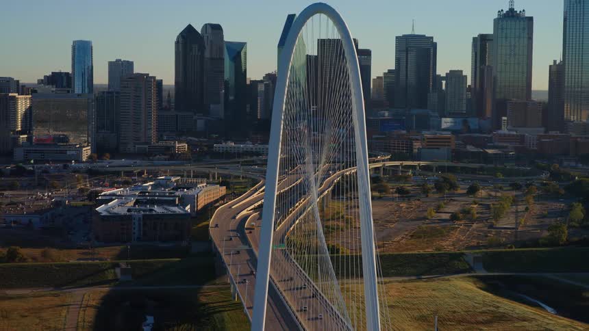 Majestic aerial footage slowly approaches the Margaret Hunt Hill Bridge, revealing the Dallas, Texas skyline at golden hour
