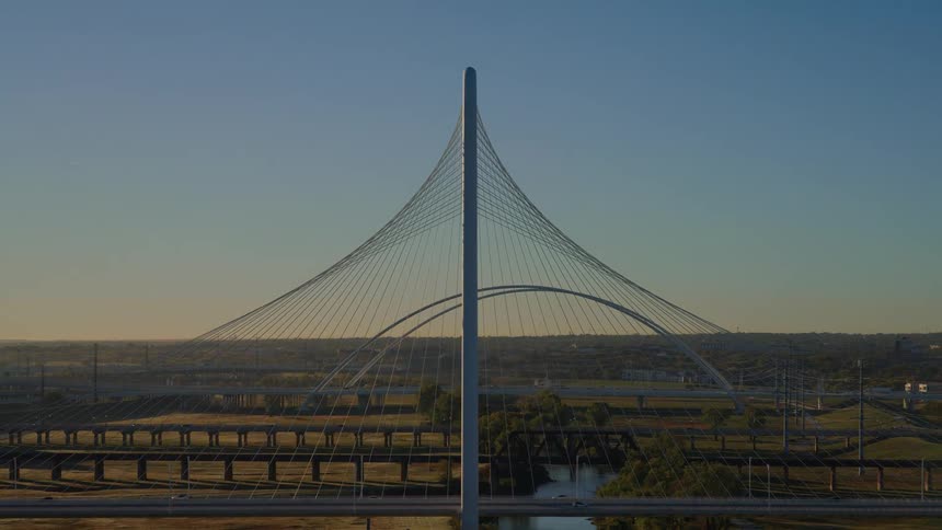 A majestic aerial view reveals the iconic Margaret Hunt Hill Bridge against the bright morning sun over the Dallas, Texas cityscape