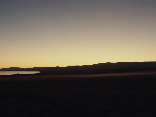 A minimalist and serene desert landscape is bathed in the warm, golden light of twilight