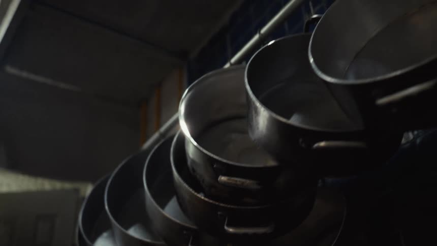 A slow-motion tracking shot of large metal cooking pots hanging in a dark restaurant kitchen