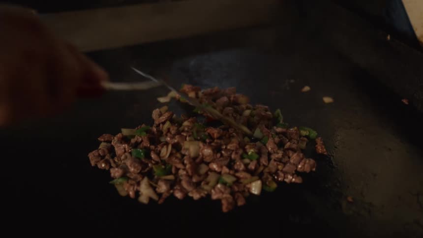 Slow motion close-up of a chef cooking diced beef with onions and peppers on a hot flattop grill