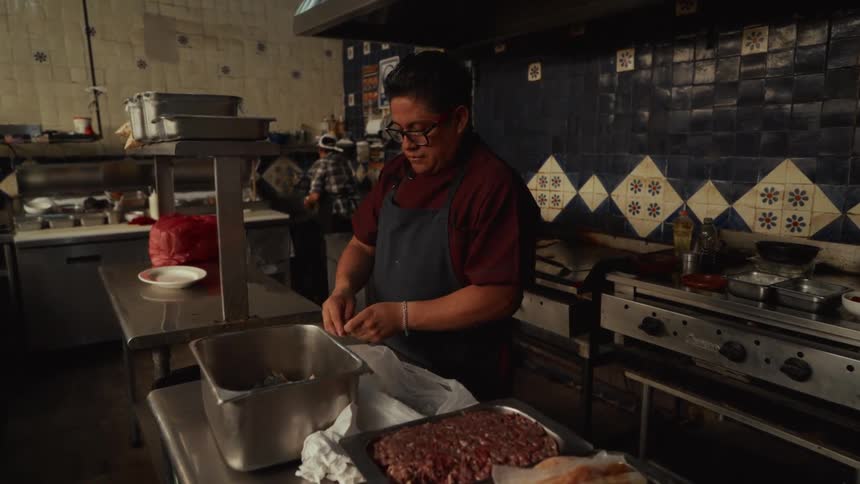 A chef meticulously prepares ingredients at a prep station in a busy, traditionally tiled commercial kitchen